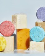 Various multicolored shampoo bars stacked on top of each other with soap suds and bubbles