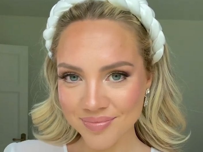 A bride with blonde hair pushed back with a thick white headband wearing natural makeup with pink blush and lipstick