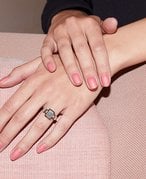 Close-up of hands with a light pink manicure and a ring on one ring finger. One hand is resting on top of the other.