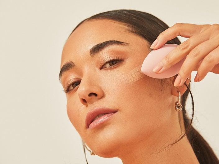 Picture of a model blending in foundation with a pink makeup sponge