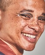 person with freckles smiling and wearing rhinestone eye makeup