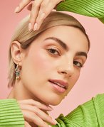 Person with a blonde pixie cut wearing a green sweater and holding their hands around their face