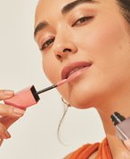 Person with dark hair applying lipstick to their lips