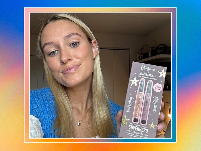 Photo of editor with long blonde hair wearing light makeup and a blue knit cardigan, holding up the IT Cosmetics x Madi Nelson Superhero No-Tug Eyeshadow Sticks Kit. The photo is collaged on a rainbow tie-dye background. 