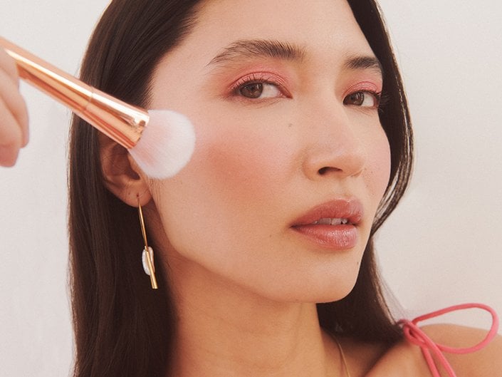 Close-up picture of a model holding a blush brush to their cheek