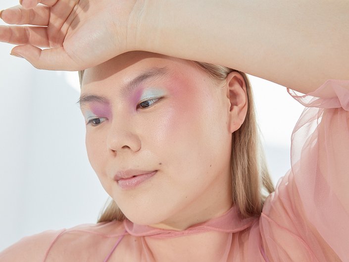 Picture of a model wearing seafoam green and lavender eyeshadow, looking off to the side and holding their hand to their forehead