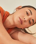 Picture of a model with dark hair in a ponytail, lying on their side