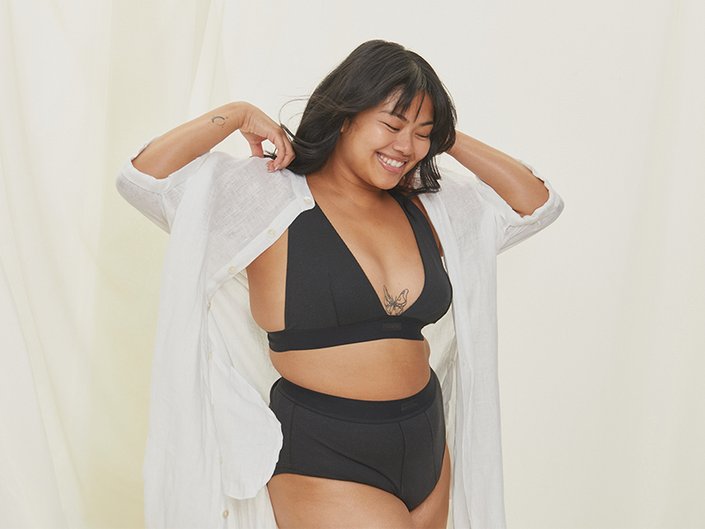 Smiling woman in black undergarments taking off a white sheer blouse